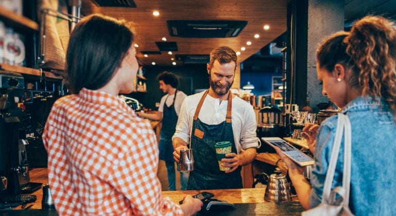 Two consumers in a coffee shop being served by a barista. This relates to the Starbucks company values example in this article.
