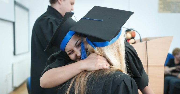 two students in graduation caps and gowns hugging