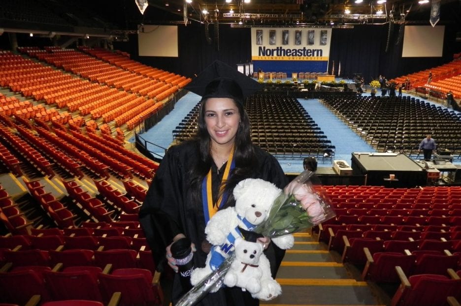 woman in graduation gown holding white bear and flowers