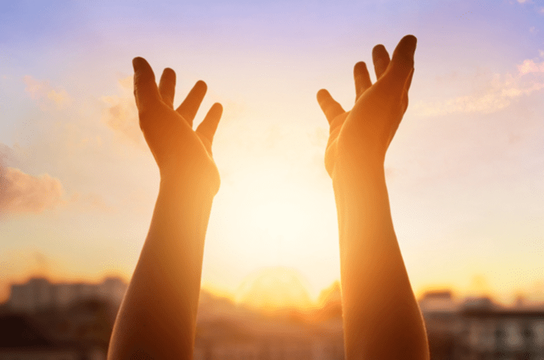 hands raised in the air between the sunset