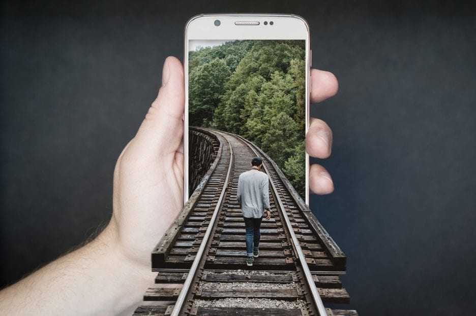 man walking on train tracks into smartphone