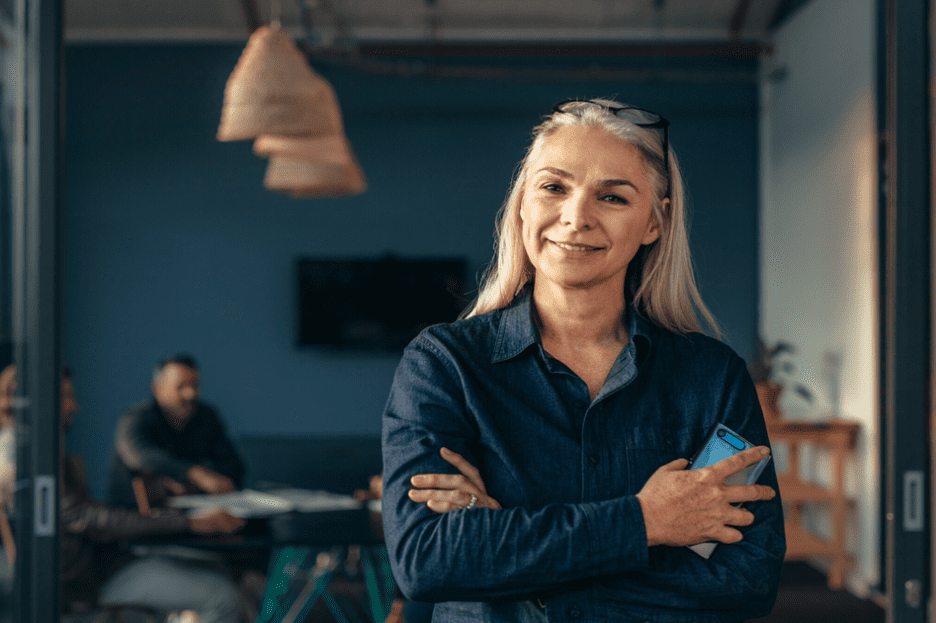 older woman holding phone with arms crossed smiling