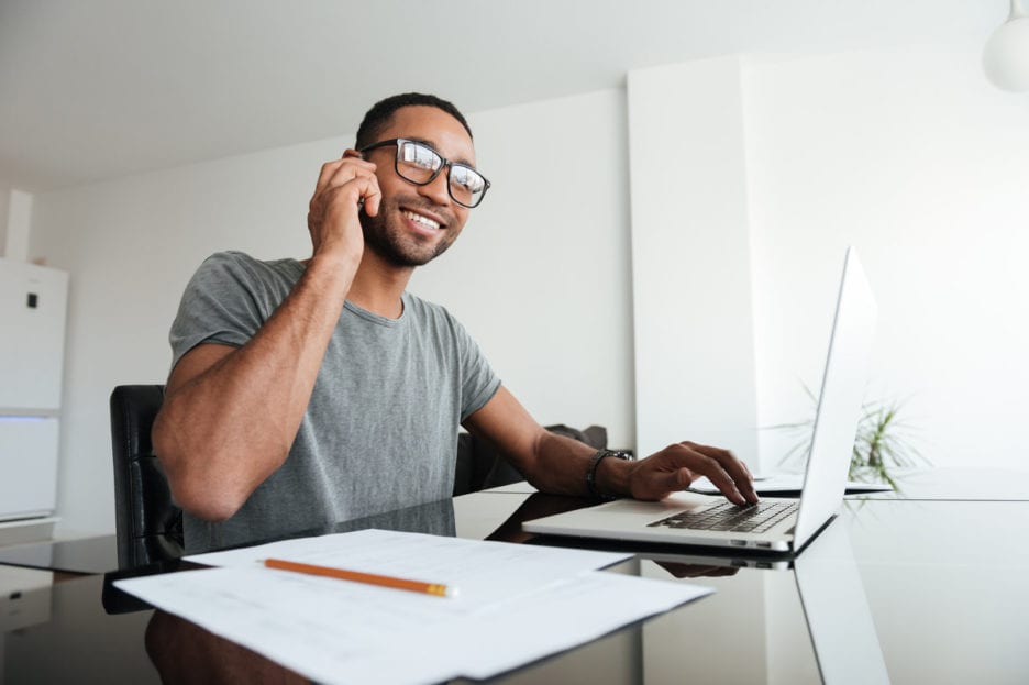 man wearing glasses on the phone with a laptop in front of him
