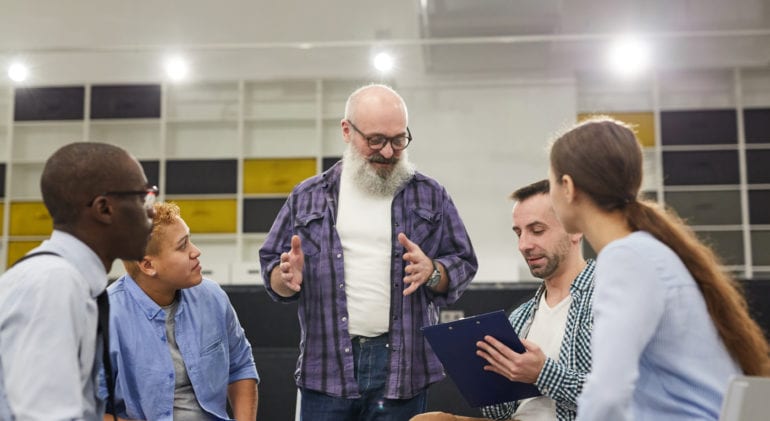 Group of people sitting in circle listening to man standing