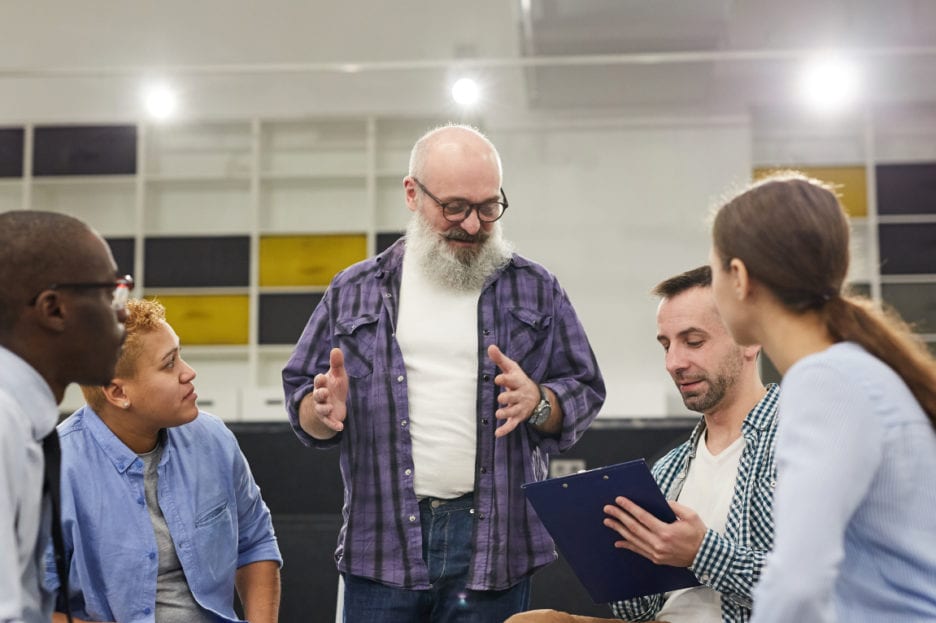 Group of people sitting in circle listening to man standing