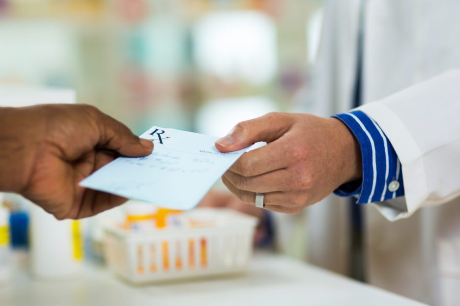 Man handing prescription paper to pharmacist